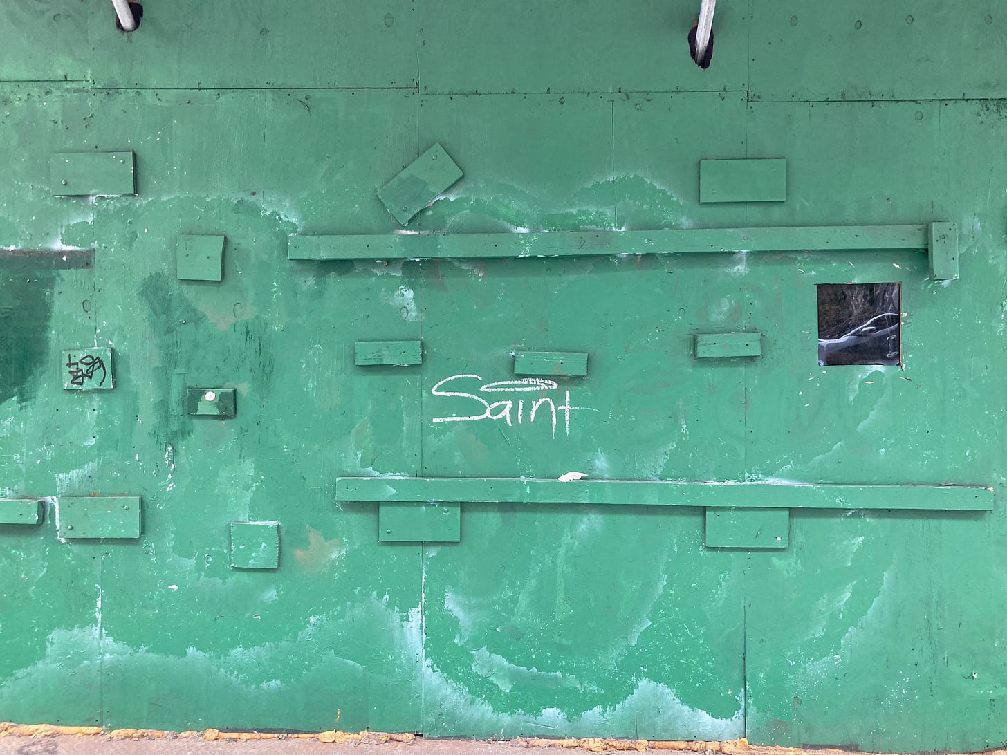 a plywood wall painted green with the word Saint painted on it, the dot in the I like a halo