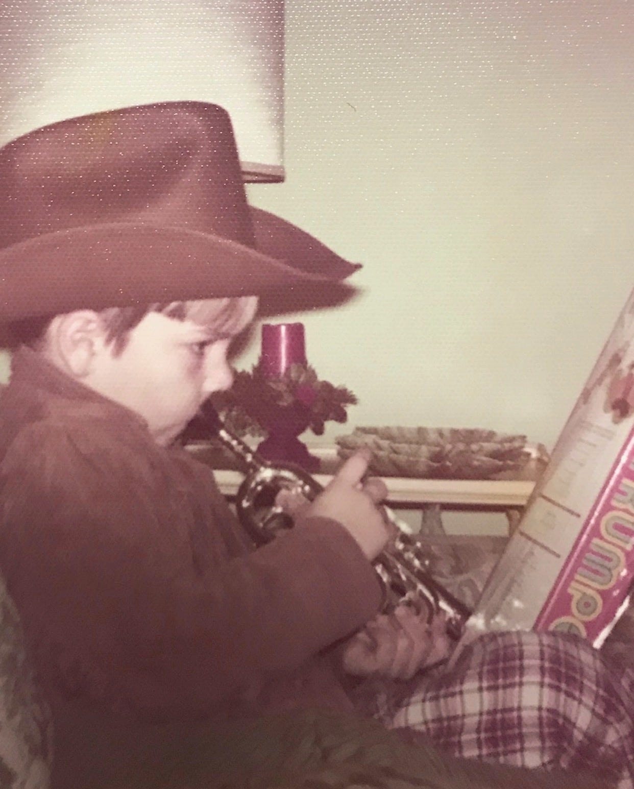 Young Jeff circa 1973 plays a toy trumpet he received for his birthday while wearing a brown cowboy hat and brown jacket.