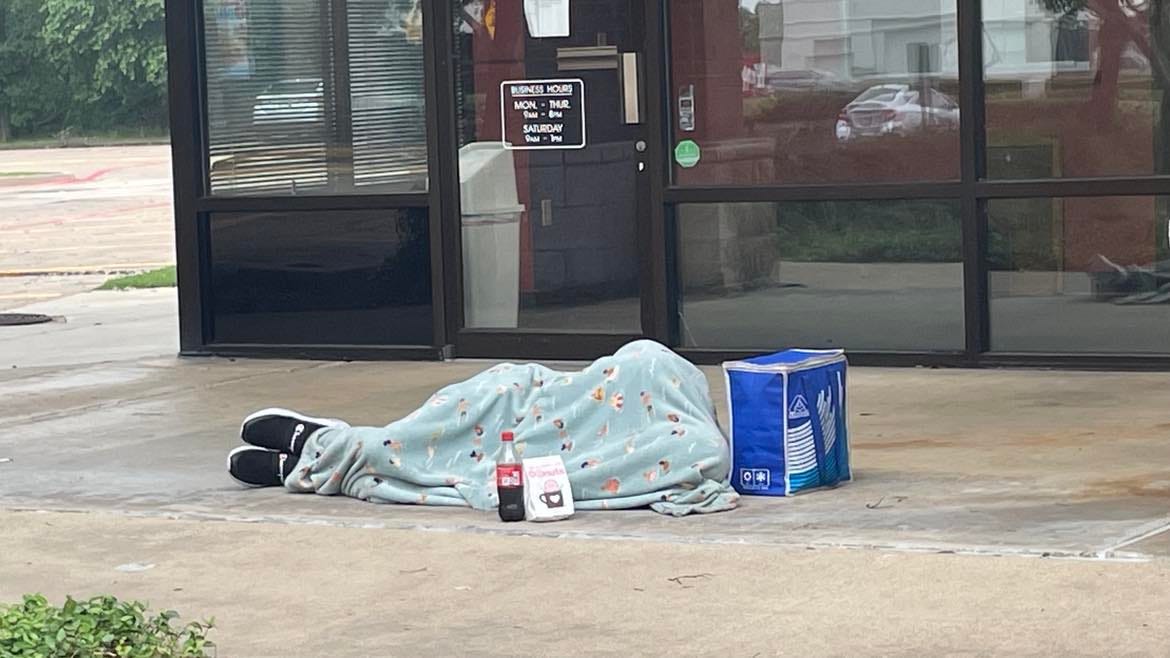 A person sleeping on a sidewalk while fully covered by a blanket