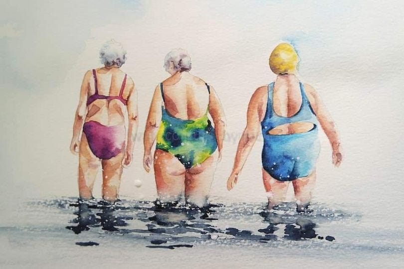 Three senior ladies in bathing suits wading into the water.