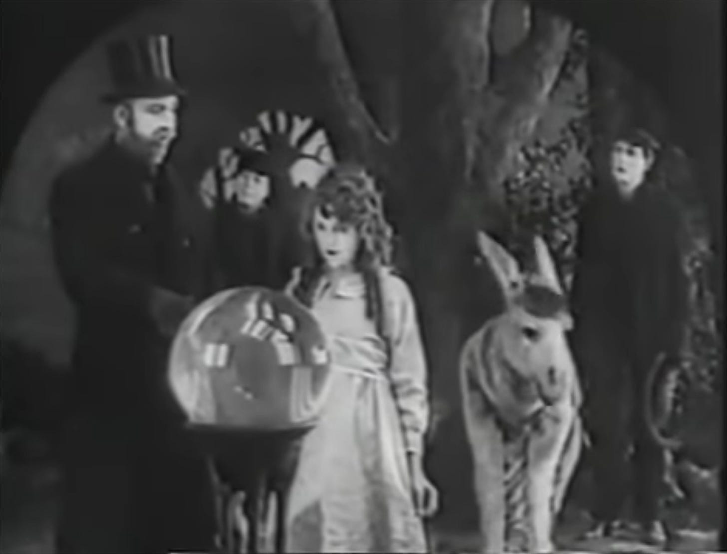 Still from 1917 fairy tale film The Poor Little Rich Girl. May Pickford, playing a child, a tall man in a top hat, a crystal ball, a person dressed as a donkey