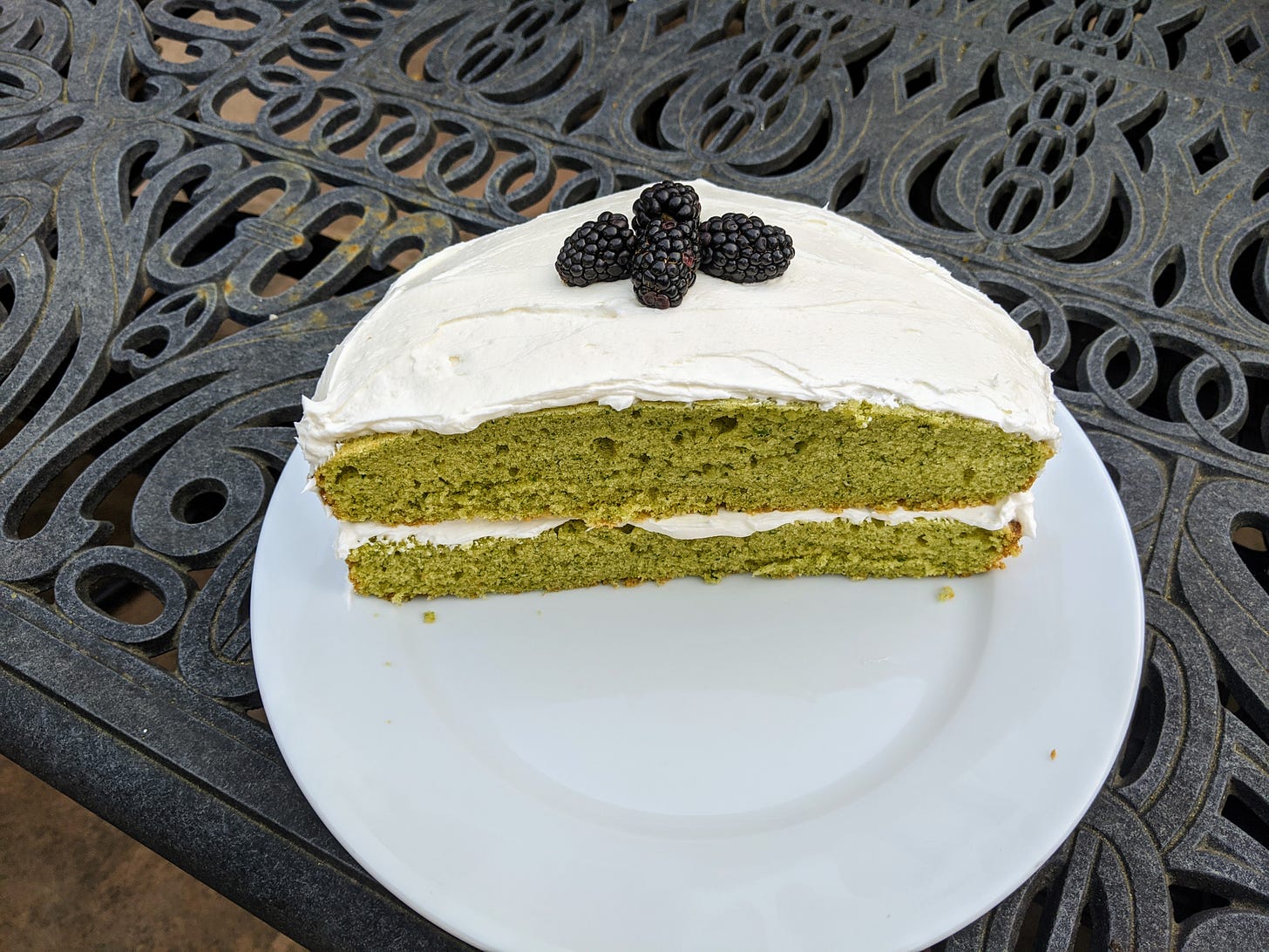 looking down on half a cake with bright green cake layers and white frosting and blackberries decorating the top