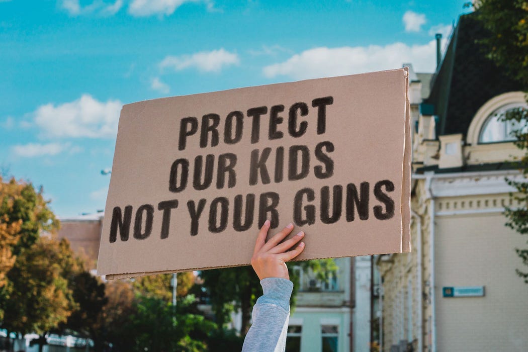 Protestor holding up a sign that reads, “PROTECT OUR KIDS NOT YOUR GUNS.”