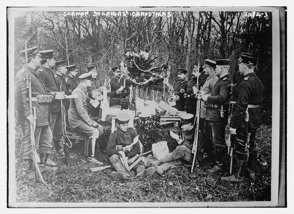 A group of fourteen German soldiers grouped around a tree that has been festooned with some Christmas decorations. It is a posed photo, with two men sat down at the front looking at, presumably, letters from home, and the other soldiers, standing either side, looking at the tree whilst holding their rifles. It's all very festive.