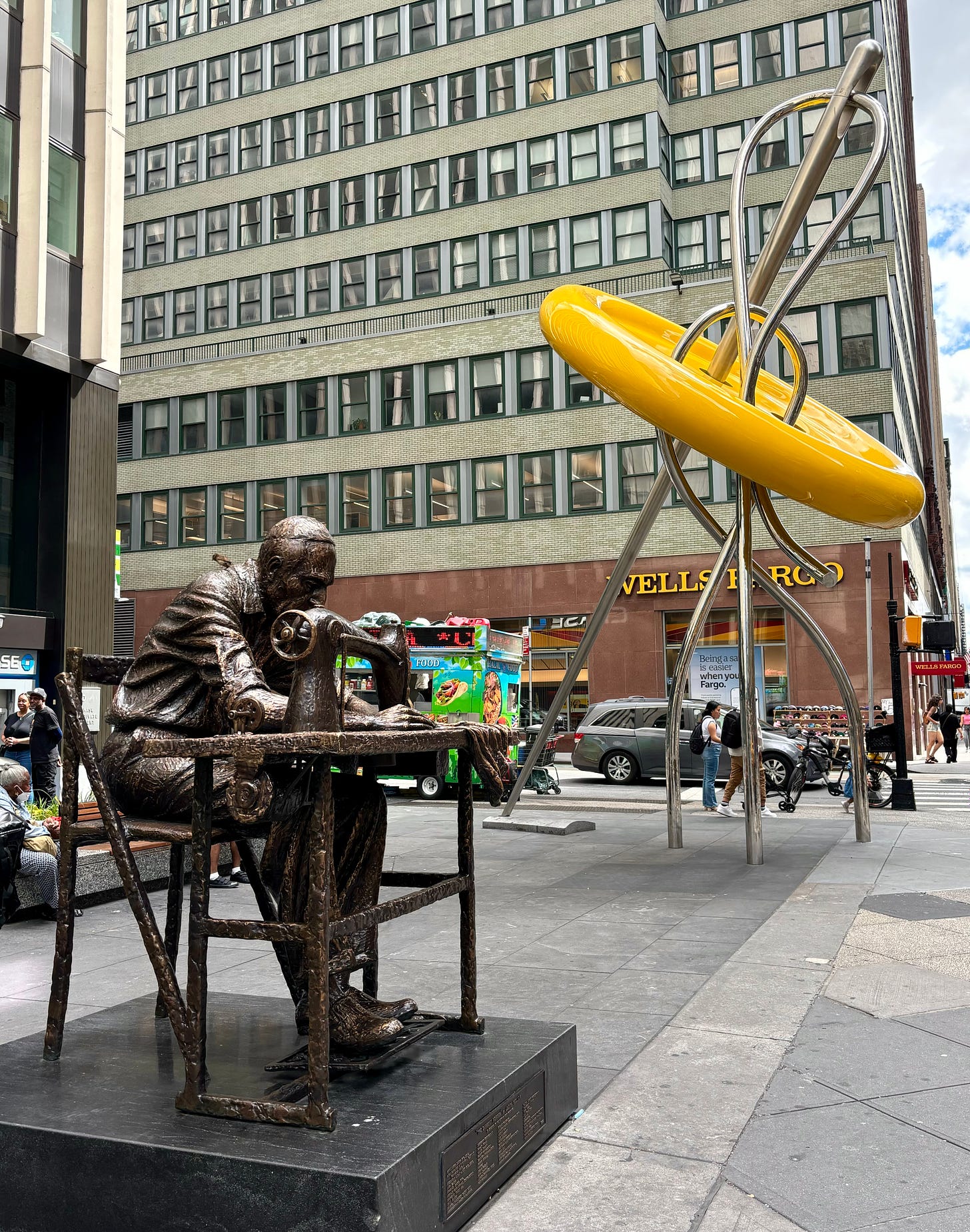 A bronze statue of an older, tired-looking man in a yarmulke bent over a sewing machine. Behind him is a monumental-sized yellow button with a silver needle and thread in it.