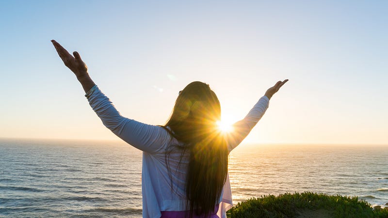 Woman raising up her arms to Heaven against the sunset
