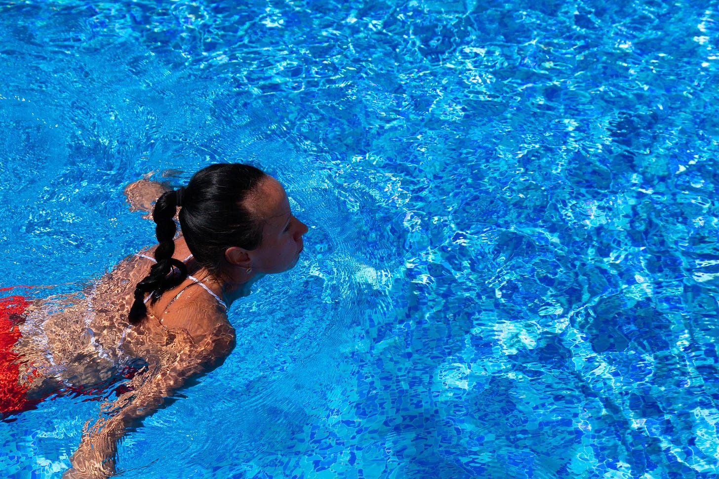 Tanned female swimming in outdoor pool.
