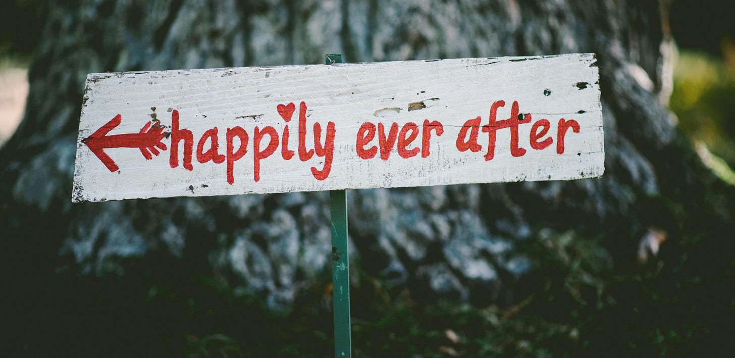 wooden hand painted sign in front of a tree. 'happily ever after' is written in red.