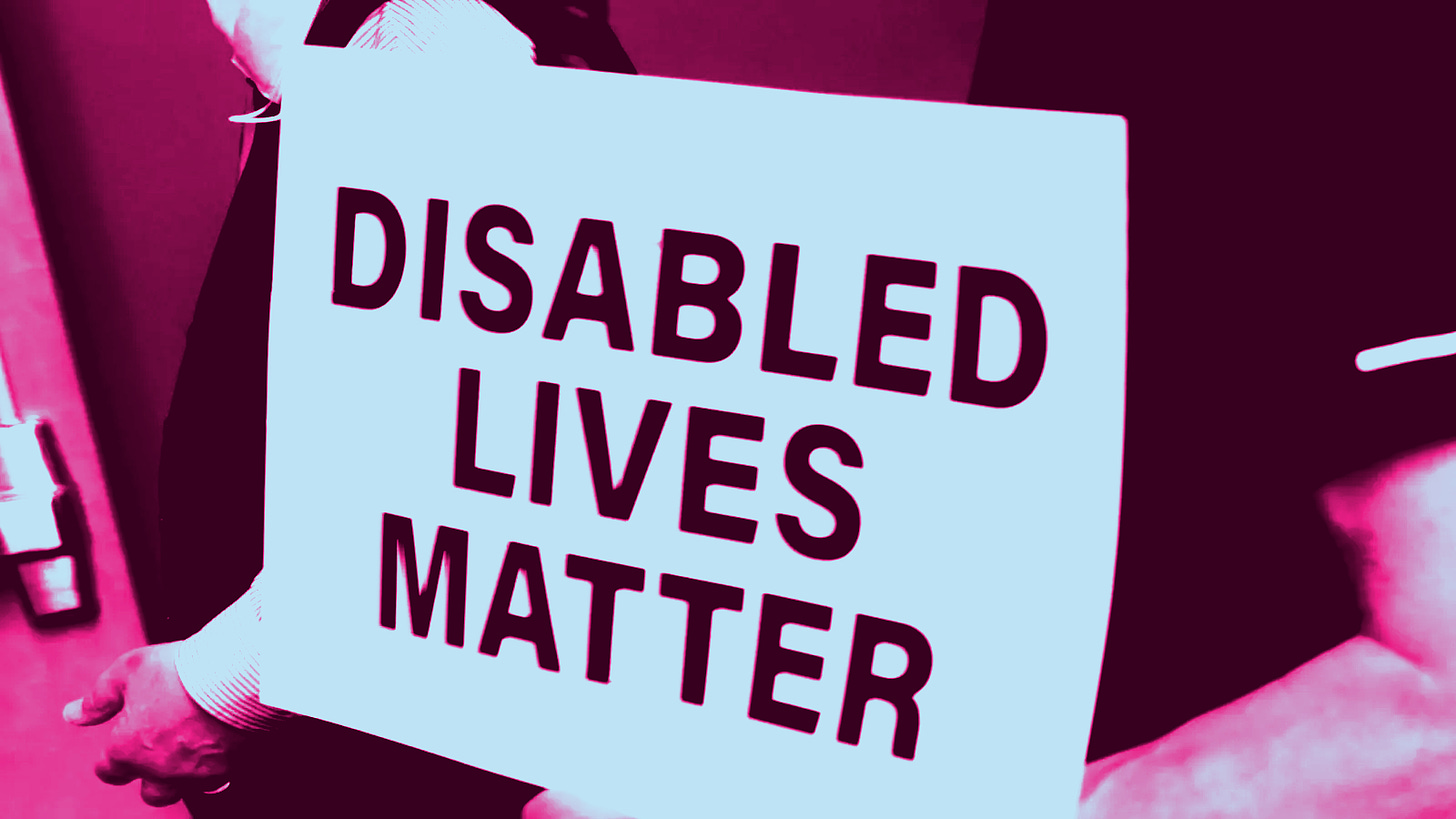Une personne tiens une feuille blanche sur laquelle est écrit "Disabled Lives Matter", "Les vies handies comptes"