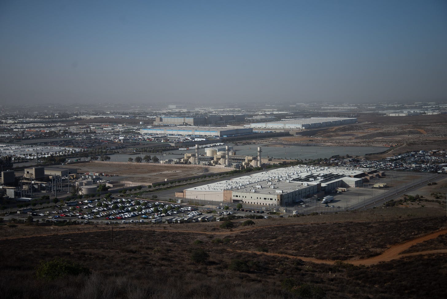Seen from a hill above, a prison with tall fences and a big parking lot lies near an Amazon warehouse Seen from a hill above, a prison with tall fences and a big parking lot lies near an Amazon warehouse