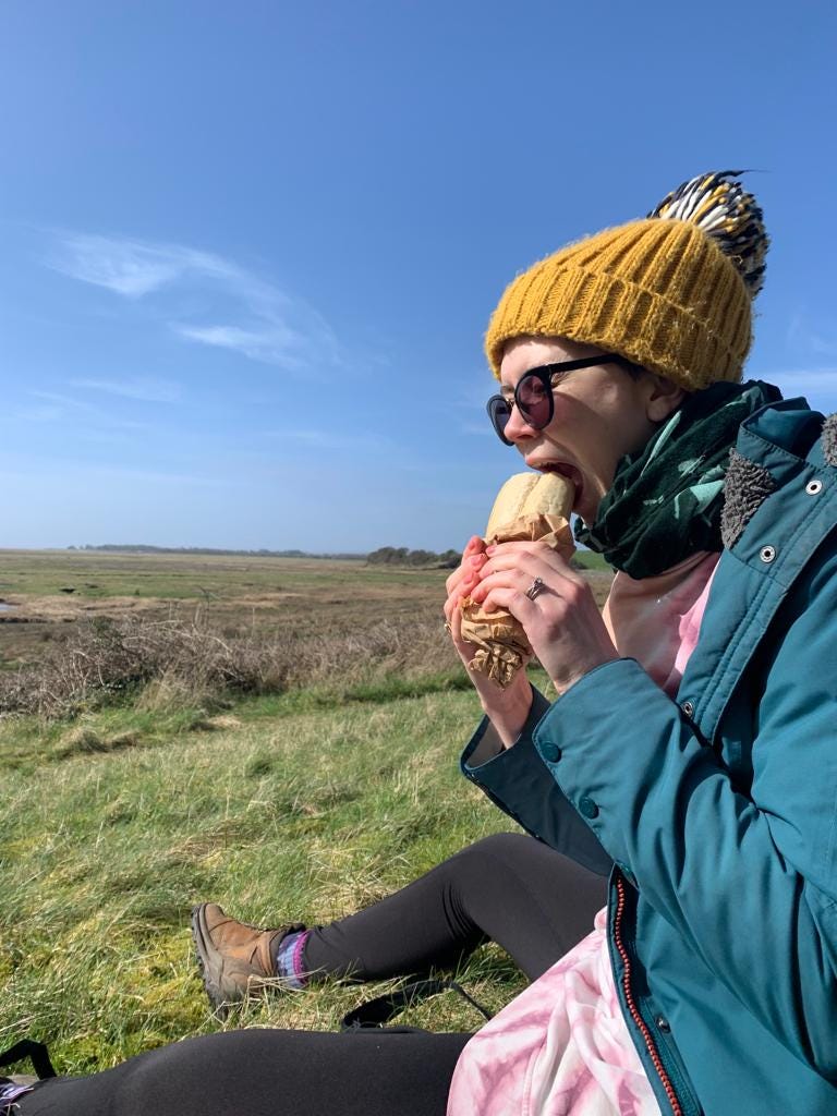 Woman bites into a sandwich at a beautiful picnic spot. Blue skies and green grass
