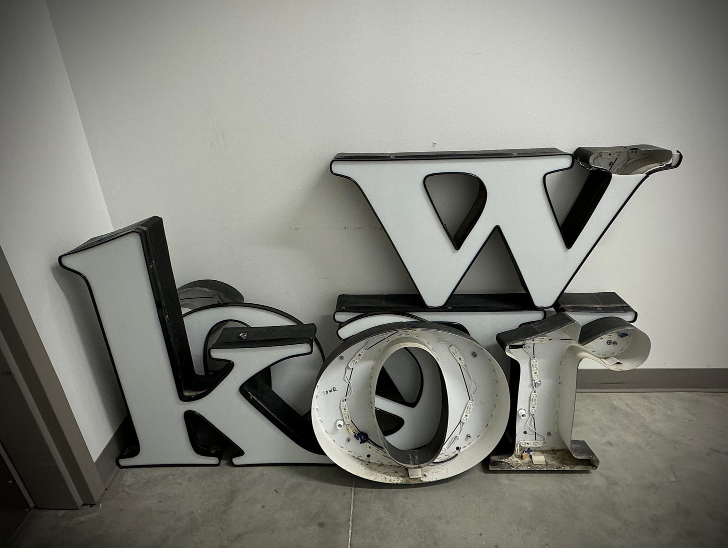 Letters of a We Work neon sign, laying on the floor of an office bldg