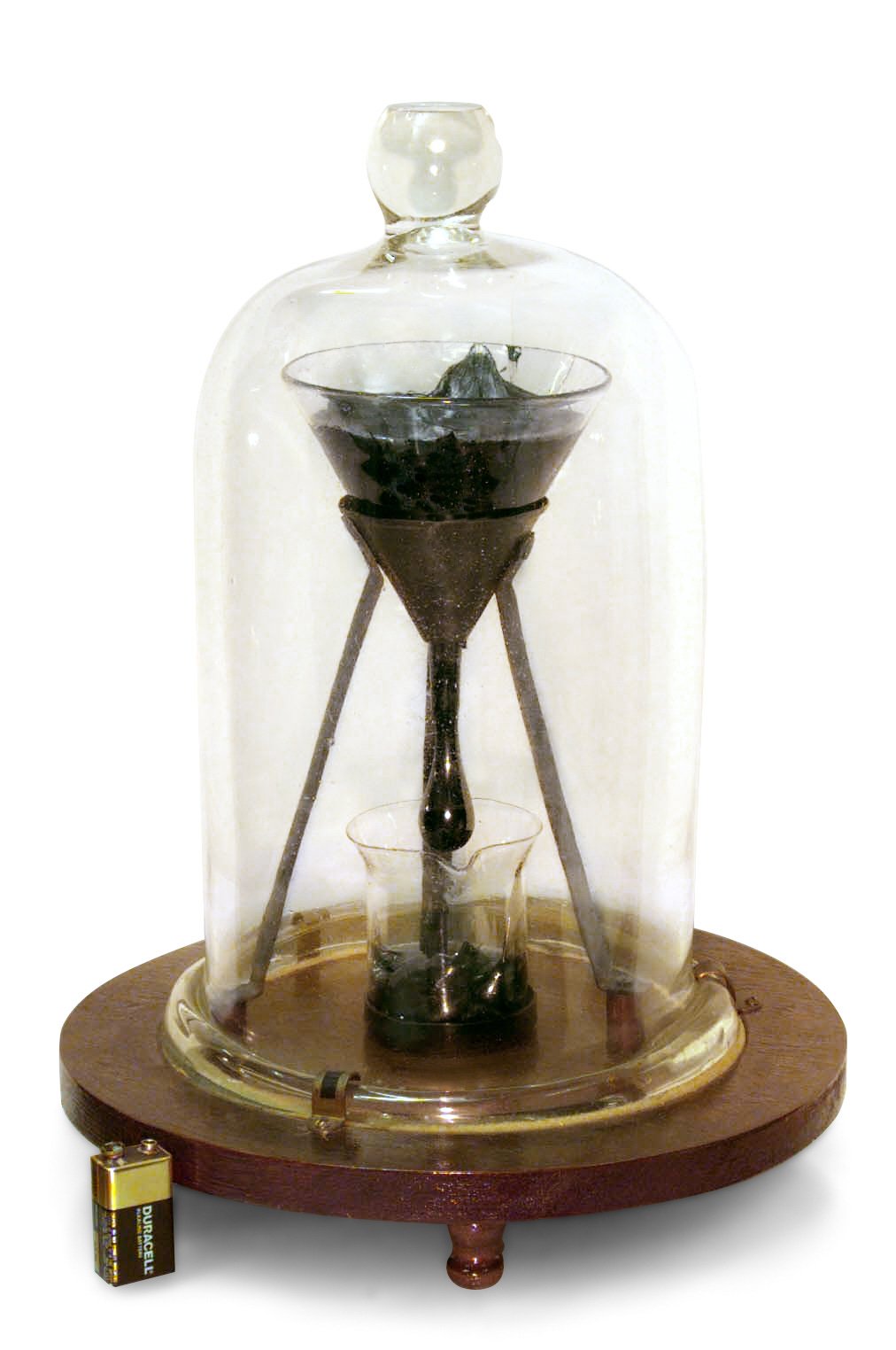 A bell jar containing a funnel containing some dark pitch which is dropping extremely slowly into a smaller jar.