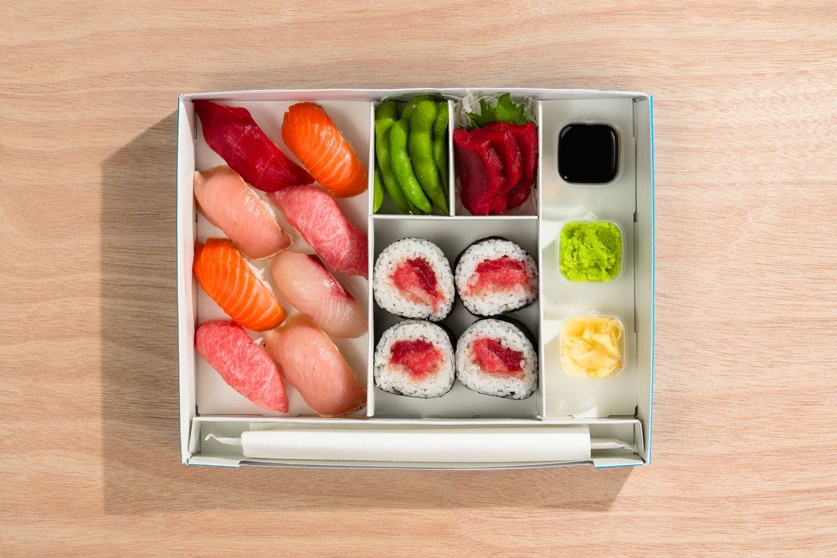 A top-down view of the Dozo sushi set in a white box with eight pieces of nigiri, tuna sashimi, futomaki, and edamame.