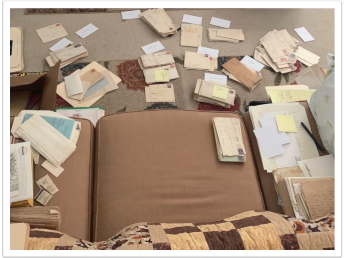 Image of a couch, seen from overhead, with piles of old letters on top and on the floor in front.