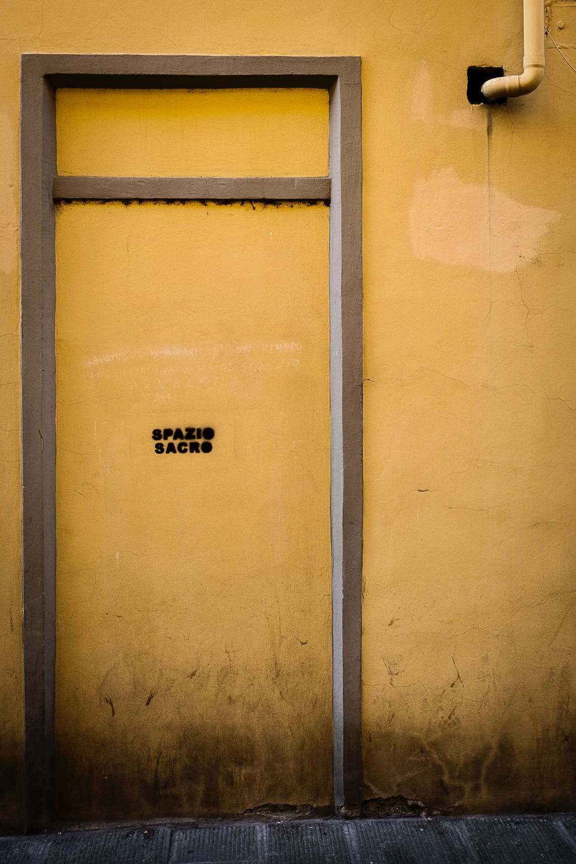 the words "sacred space" in Italian are written on a yellow wall in Firenze, Italia