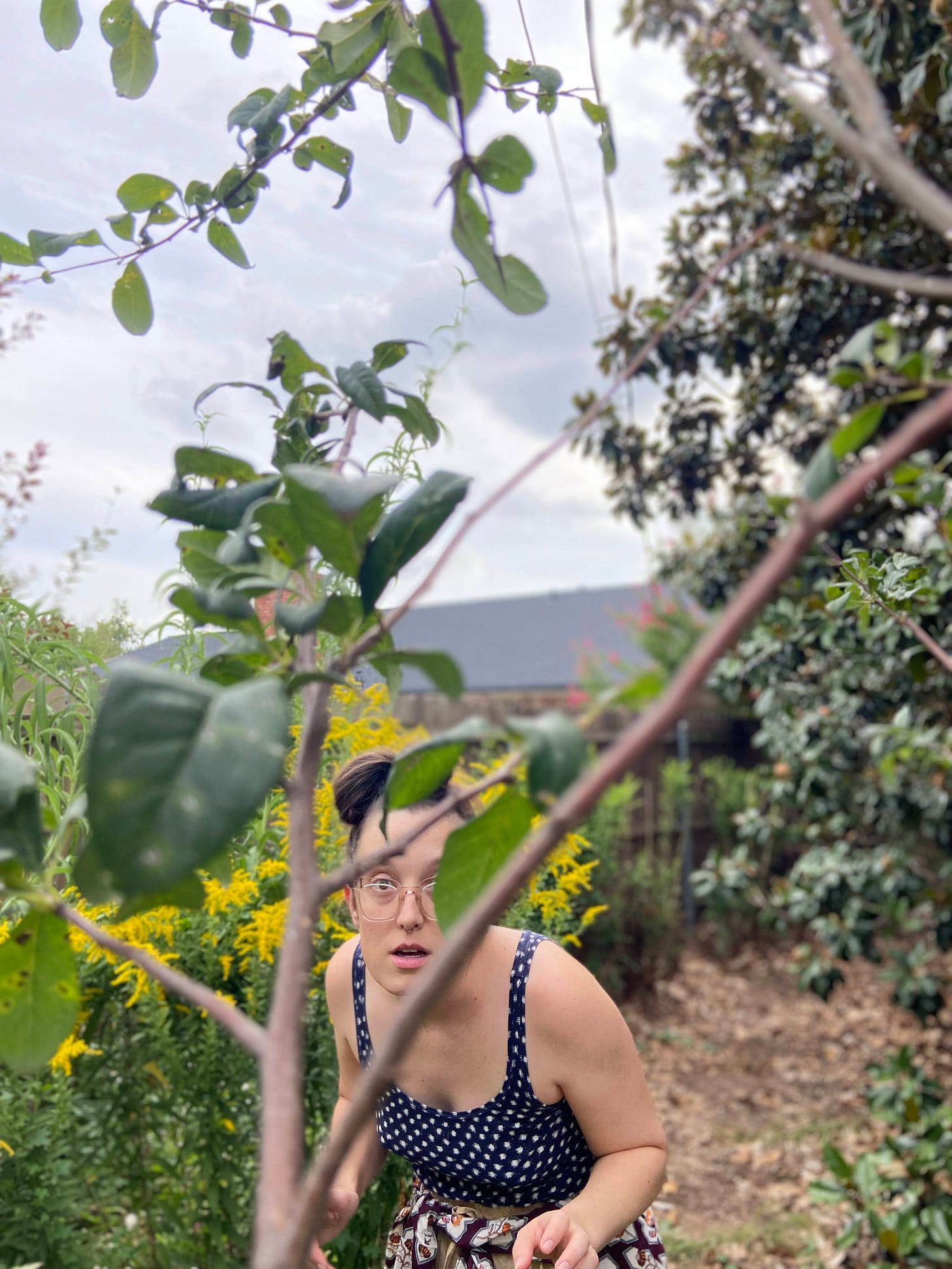 woman in the garden looking through branches with goldenrod blooming behind