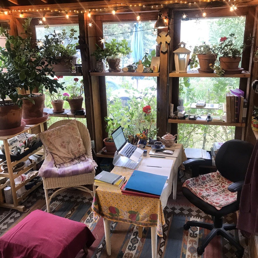 Garden office room with desk covered in notebooks, twinkle lights, and plants on shelves. 