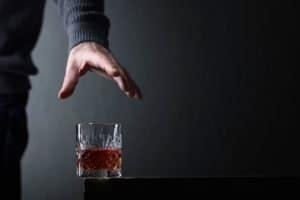 Man's hand reaches for a glass of alcohol. Conceptual image on the subject of alcoholism. Copy space for your text.