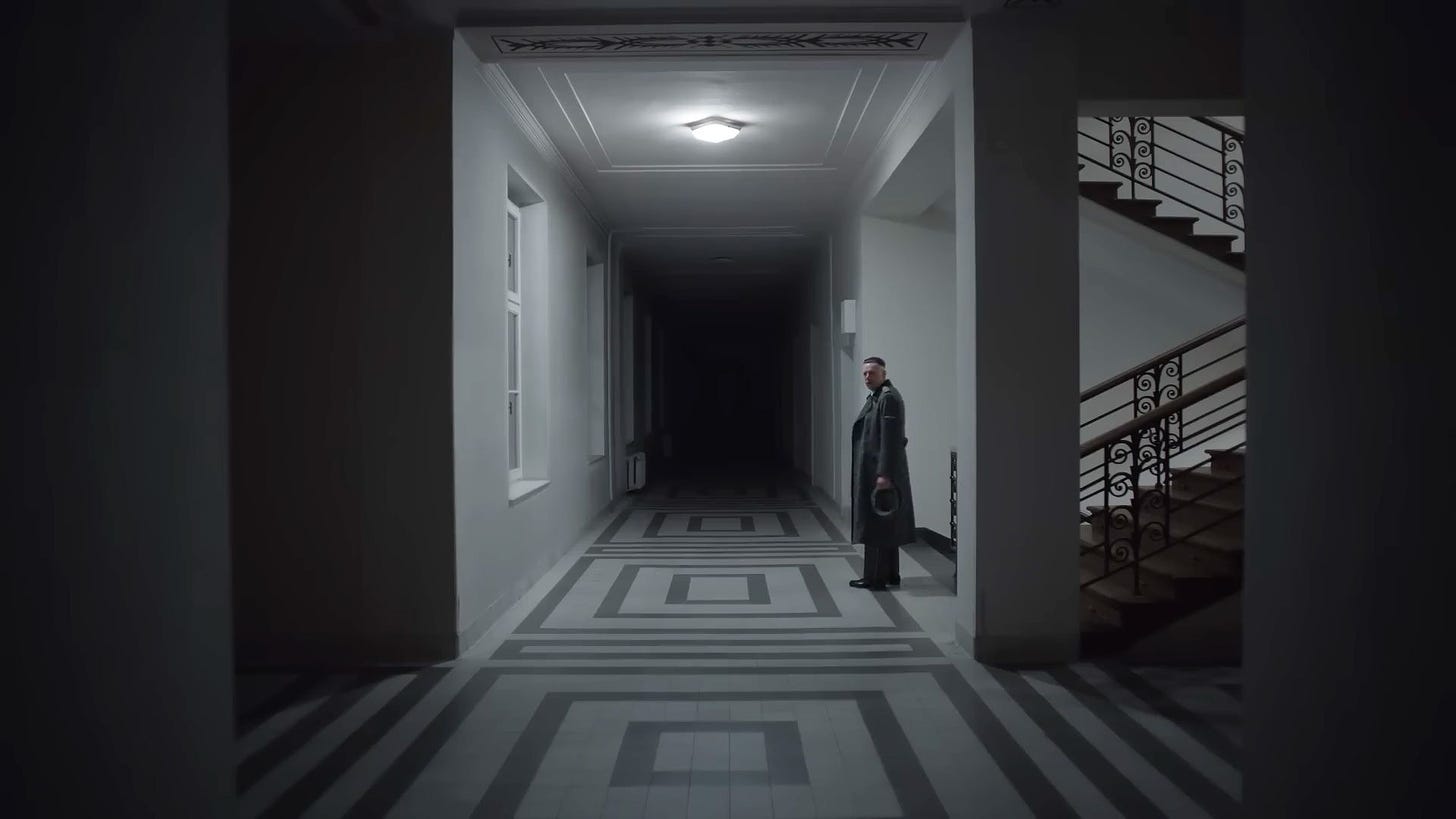 Movie still from The Zone of Interest. A man stands alone in a dimly-lit hallway.