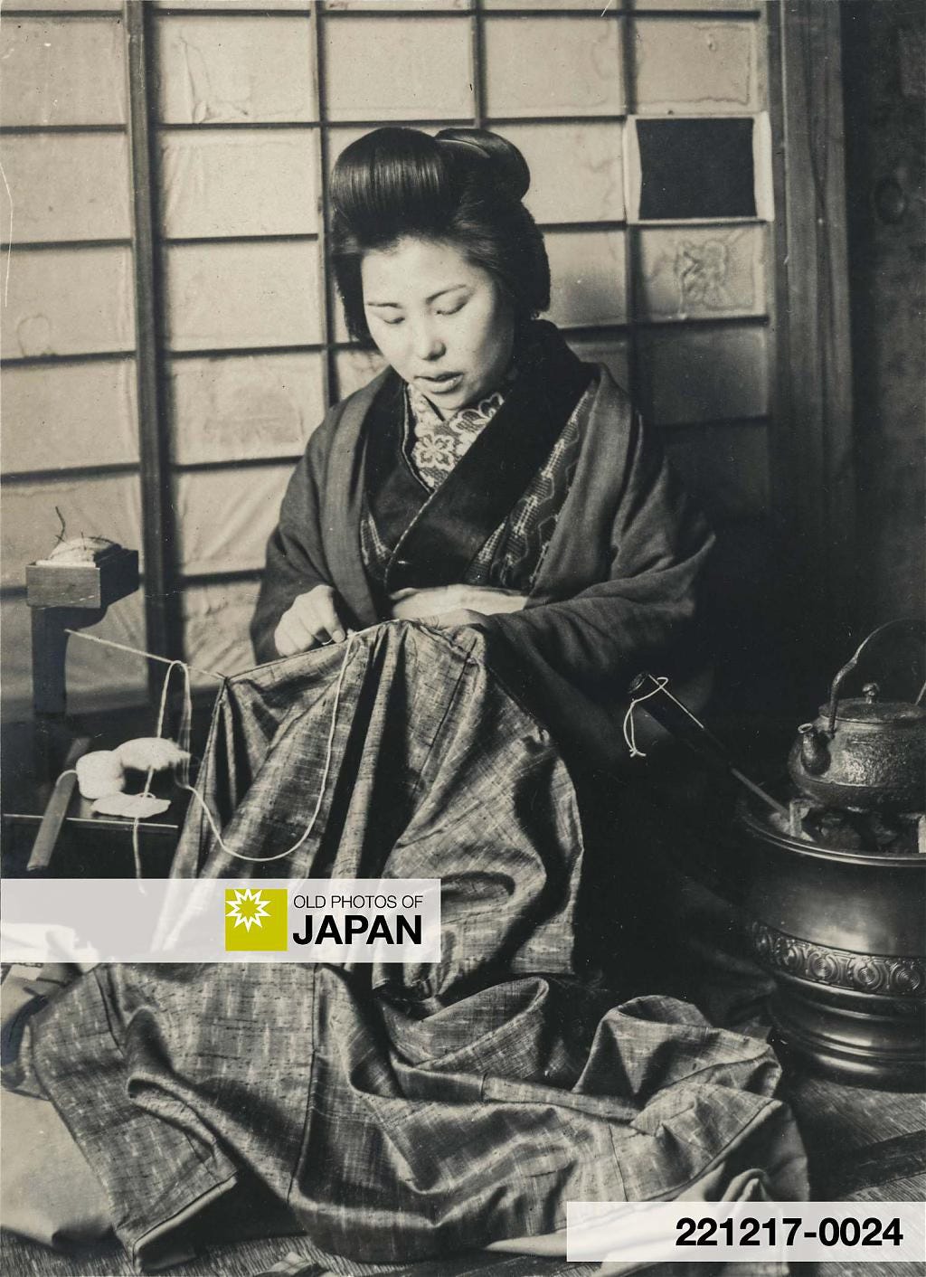Japanese woman mending clothes next to a hibachi, 1910s