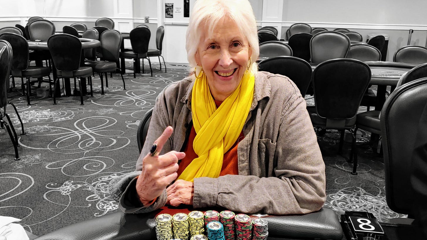 Photo of Donna Blevins when she came in first after a long tournament. She is sitting at a poker table with all the chips in front of her. She is in a grey flannel shirt and yellow scarf.