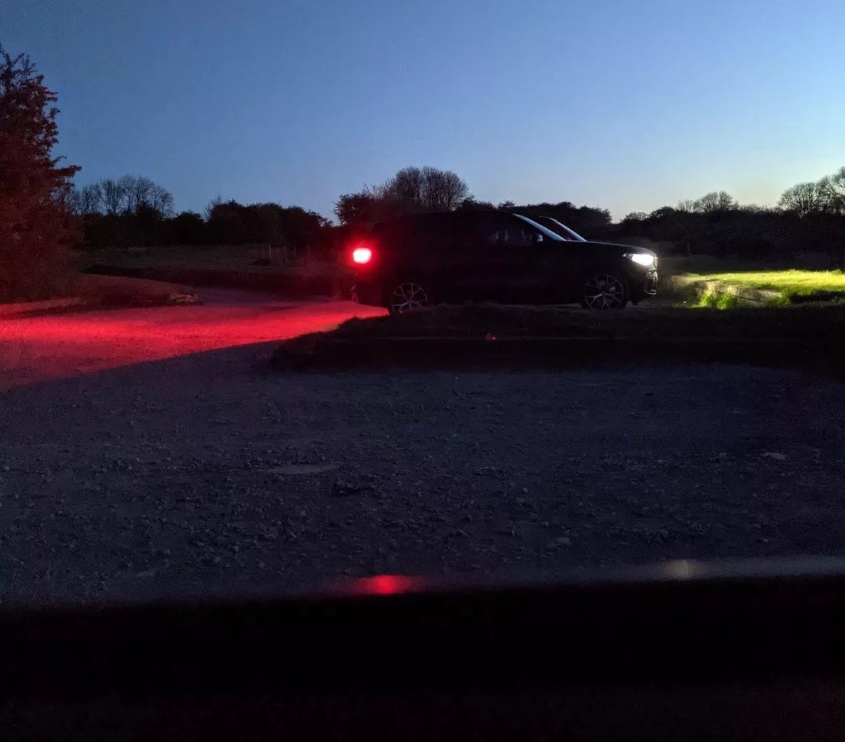 view from a car dashboard of two other parked cars with headlights on, at dusk