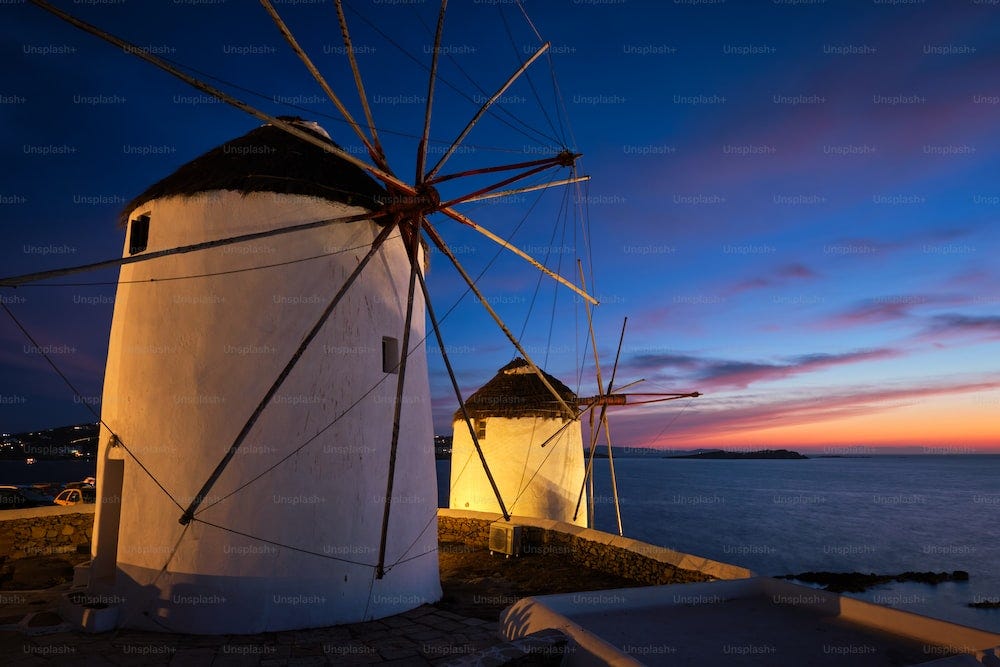 Scenic view of famous Mykonos Chora town windmills. Traditional greek windmills on Mykonos island illuminated in the evening, Cyclades, Greece. Walking with steadycam.