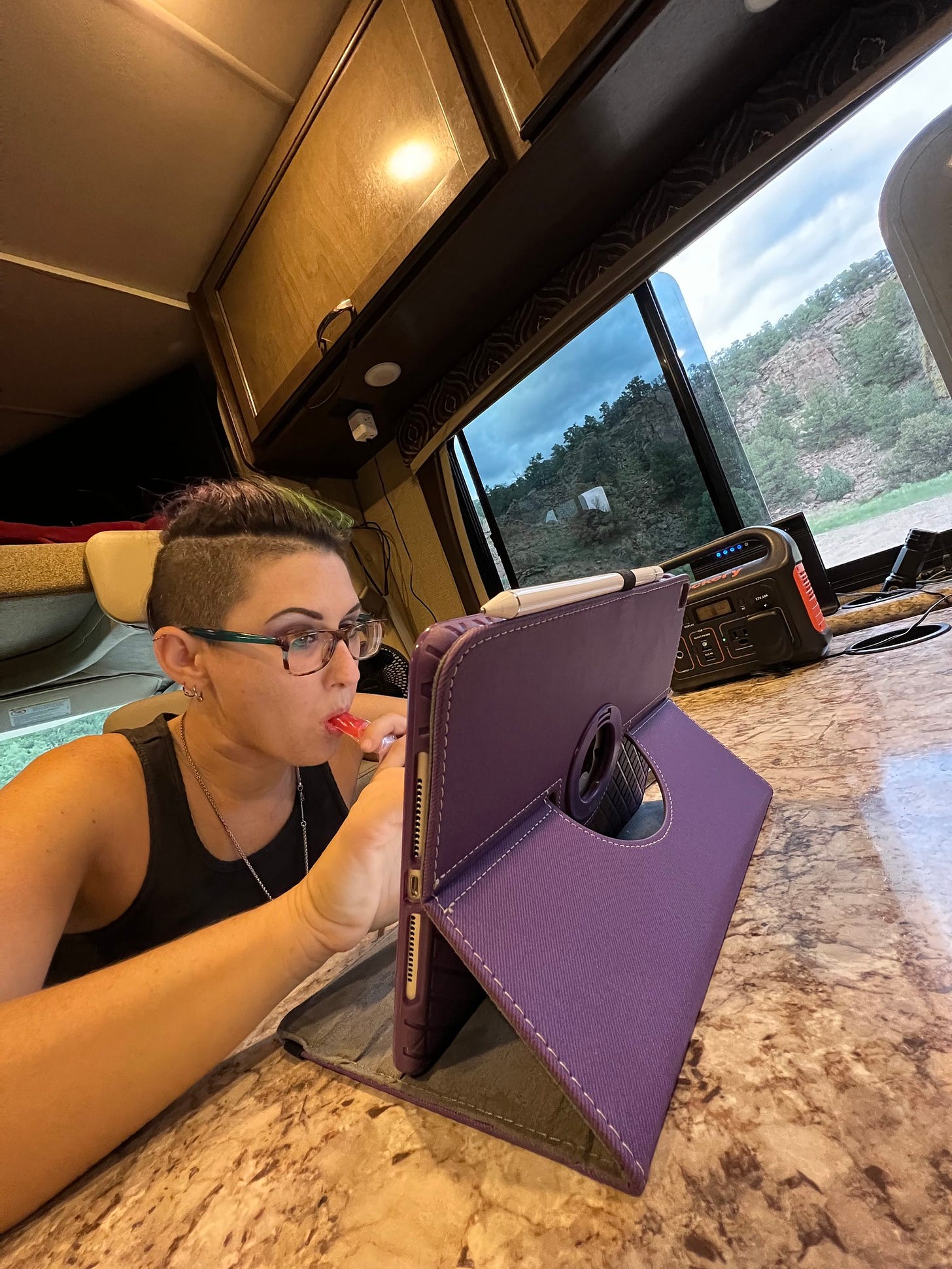 photo of Lyric  in their RV typing in the iPad and eating a Popsicle. 