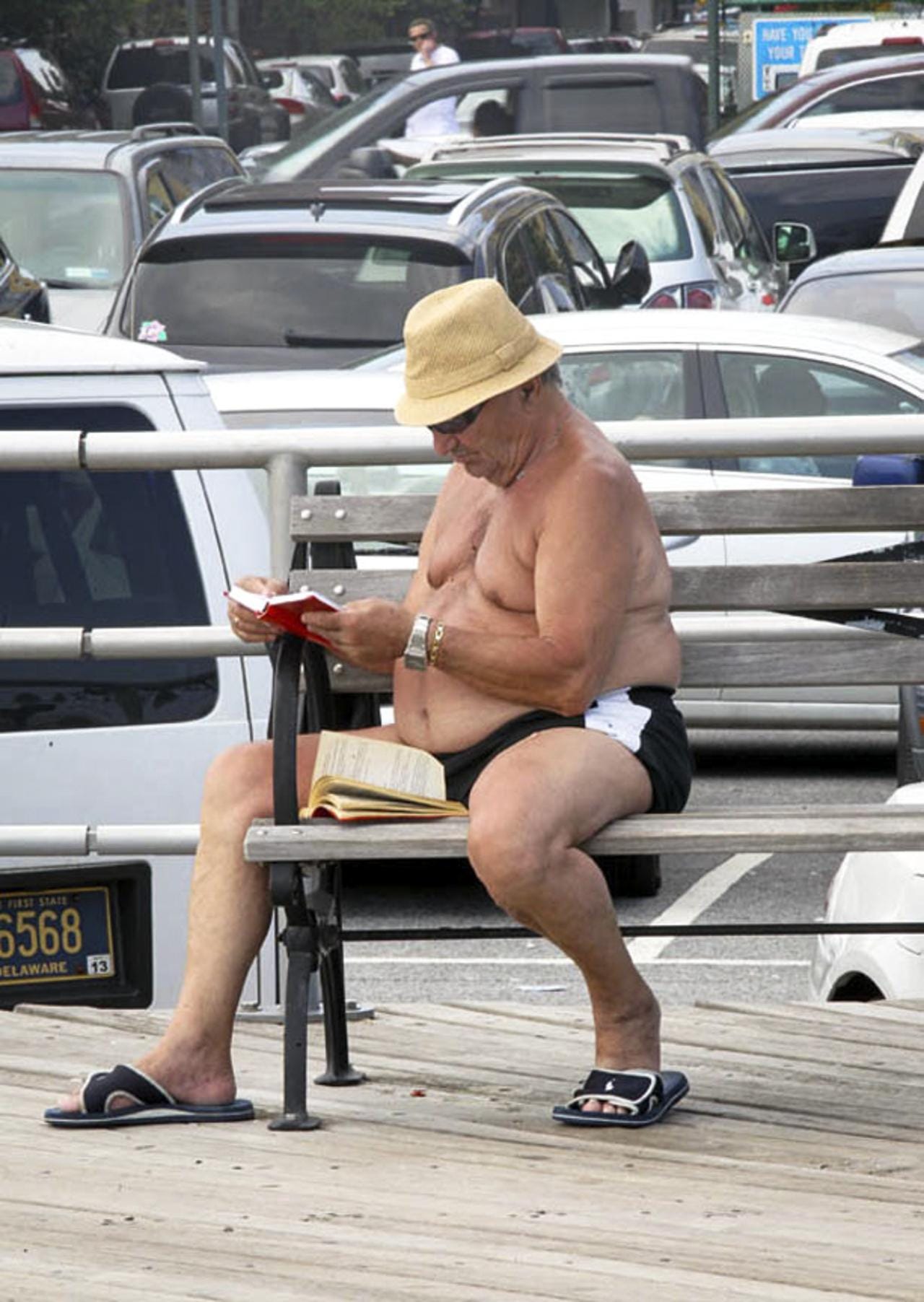 A shirtless man on the Brighton Beach boardwalk reads two books.