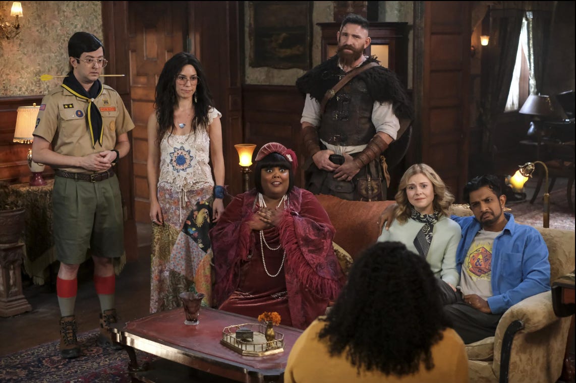 A man in a scout uniform with an arrow through his neck, a hippie, a viking, a woman in a flapper outfit, and a married straight couple in a room in an old-looking house