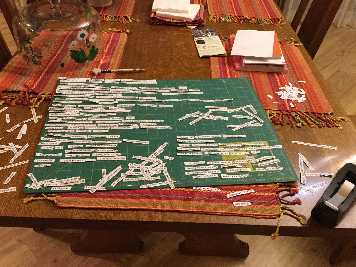 A fabric cutting board on a table where words cut from paper are being organized into poems.