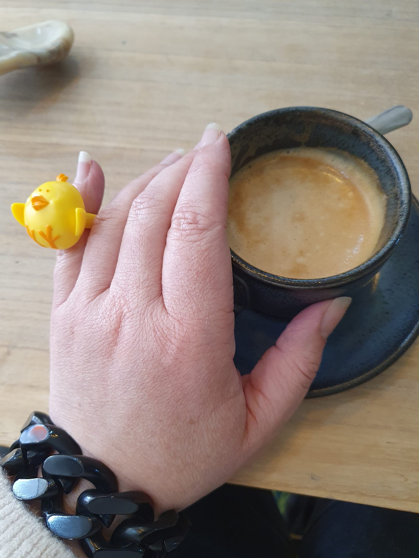 A hand wearing a large yellow plastic chick ring that is too small and holding a cup of coffee.