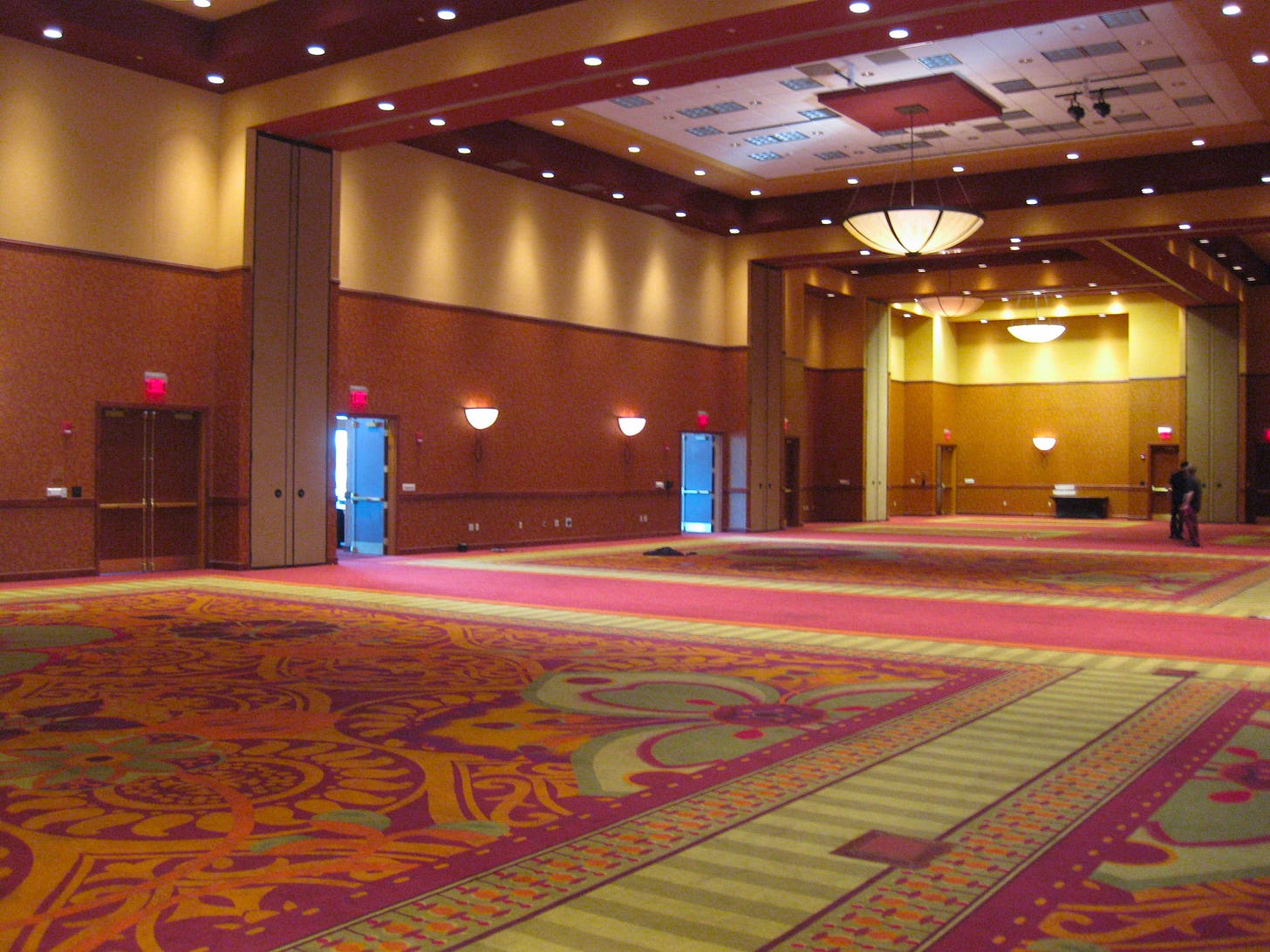 uninspired conference ballroom with no windows and a large pattern red and gold rug.