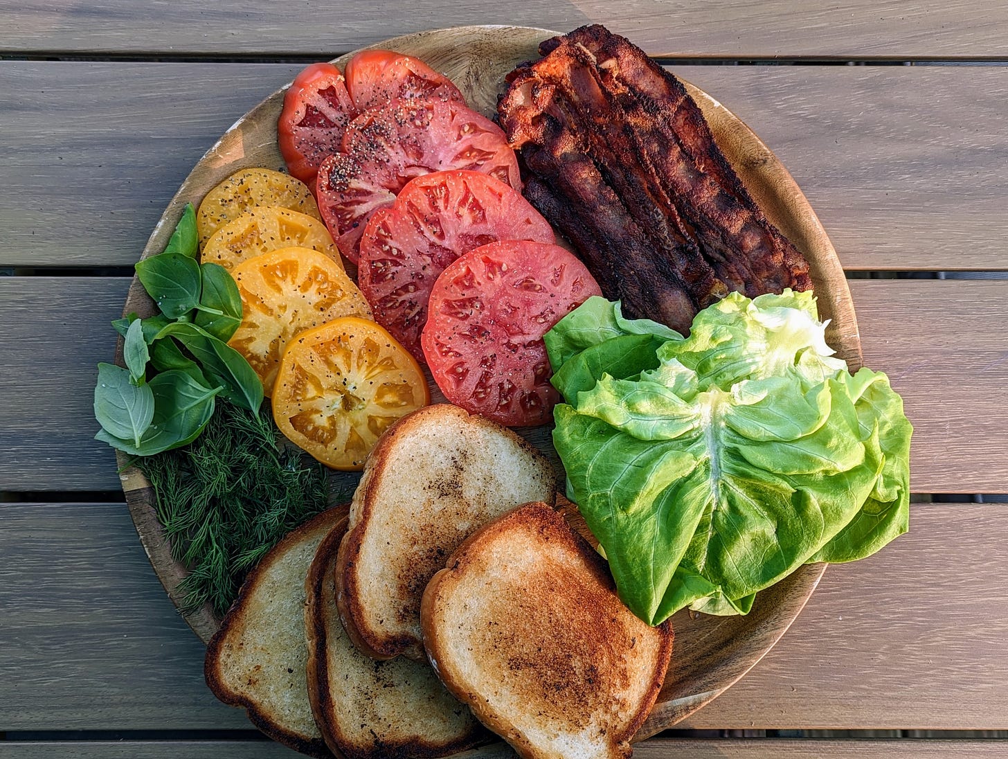 A vibrant and colorful blt board with bacon, lettuce, tomatoes, bread, and herbs.