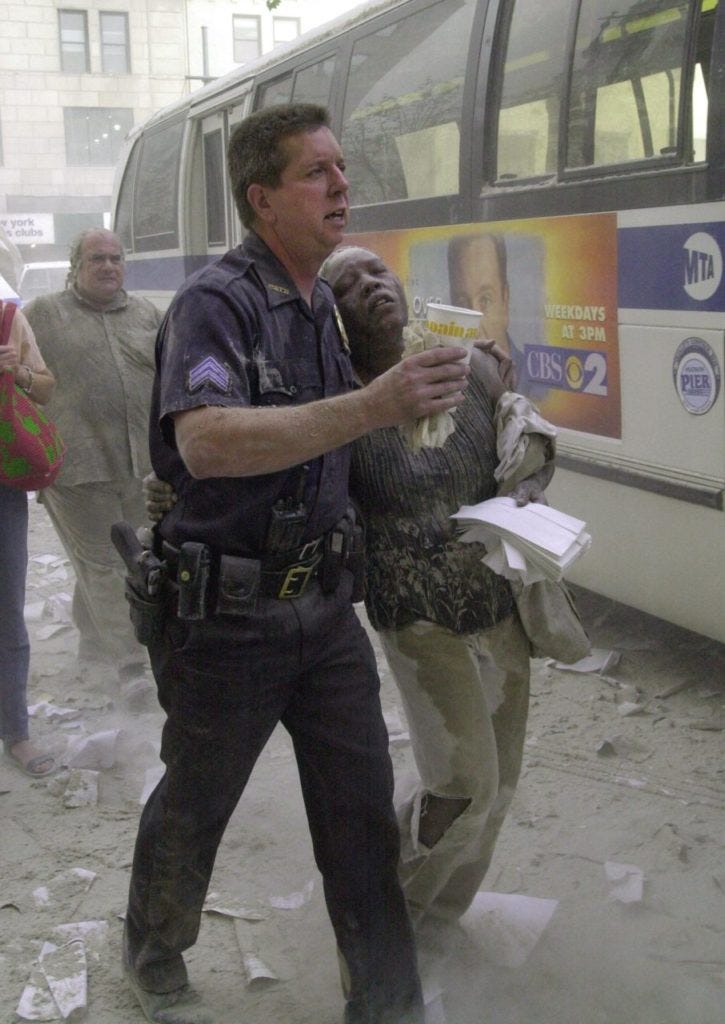 A police officer helps a woman to a bus after she fled the area near the World Trade Center towers 11 September, 2001, in New York. Two planes crashed into each building and the tops of each tower later collapsed AFP PHOTO/Stan HONDA (Photo credit should read STAN HONDA/AFP/Getty Images)