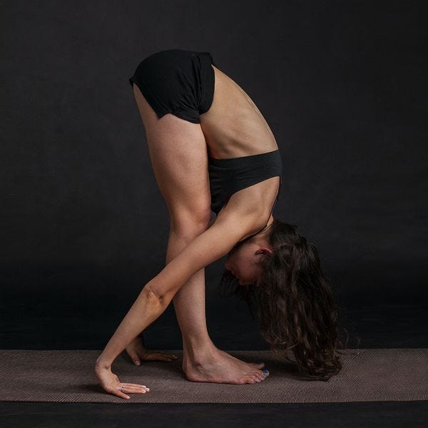 Person standing bent over stretching past their feet, with palms on the ground behind them