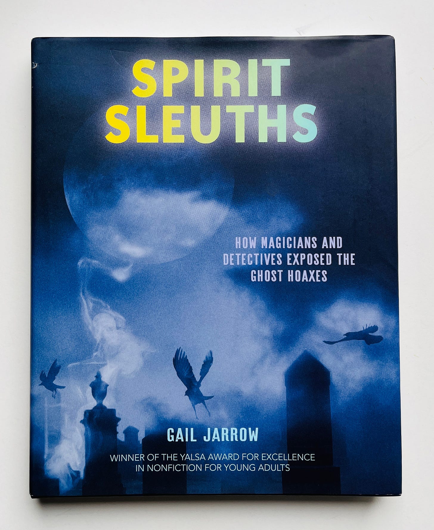 The cover of a book with a spooky scene of a graveyard, mist, a giant full moon, and black birds flying around