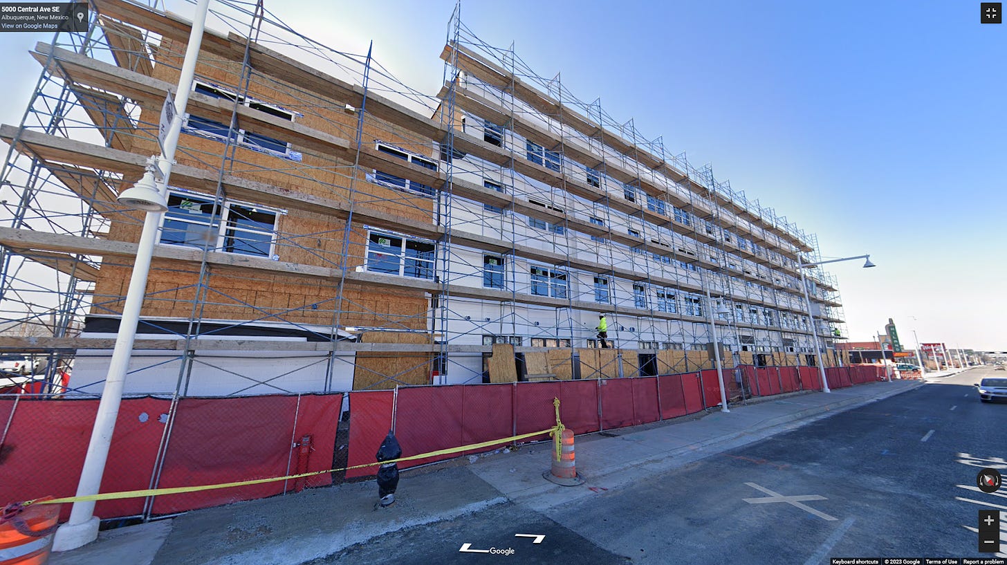 A partially constructed building with construction fencing and scaffolding. It is a tall building with future apartments over future retail space.