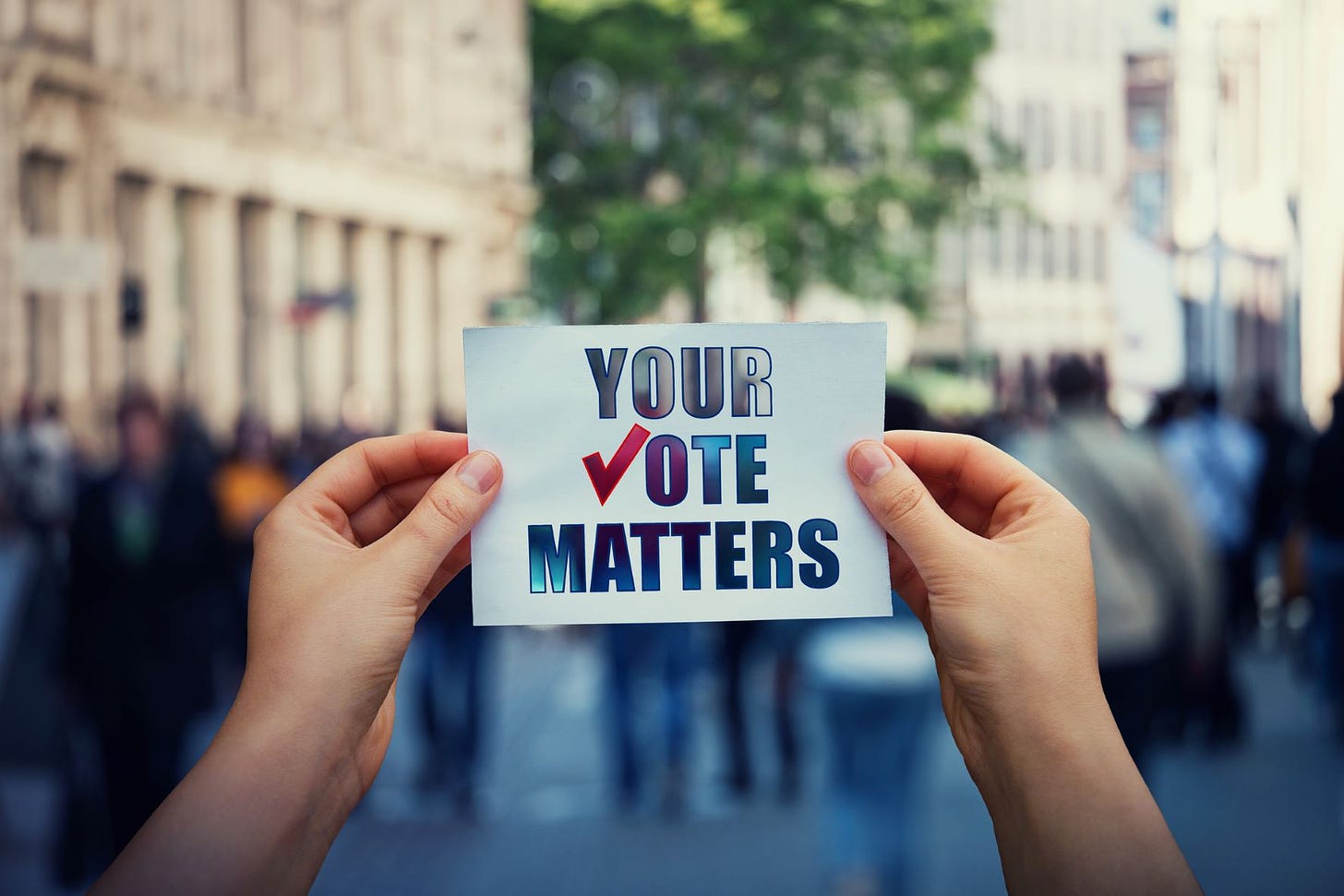 Hands holding up a sign reading, "Your Vote Matters." The "V" in "Vote" is a checkmark.