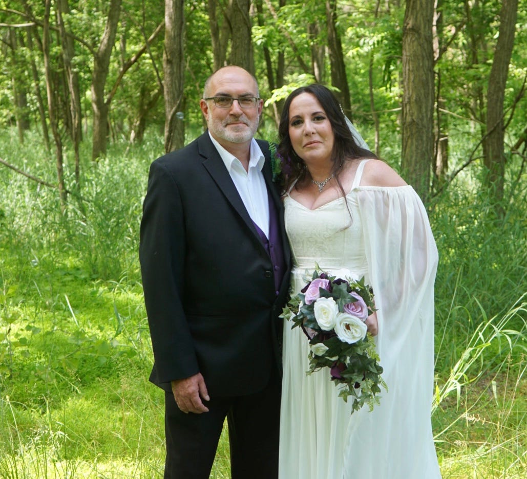 Brian and Mary standing in a forest in their wedding clothes.