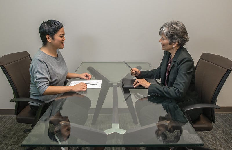 An Asian woman sitting at a table being interviewed for a job.