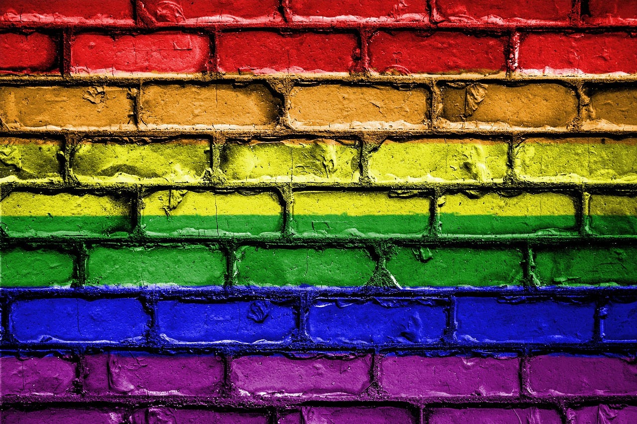 image of a brick wall that seemingly has the colors of the LGBTQ+ rainbow flag painted on it