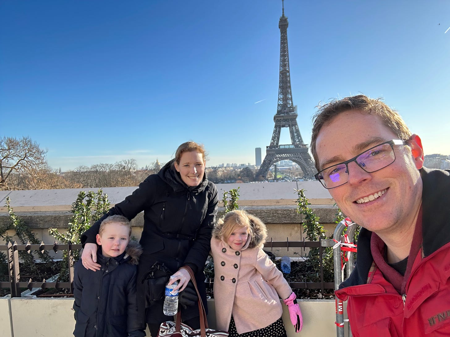 Picture of my family, my wife with kids, with my in the foreground in selfie pose, in the background the Eifel tower.
