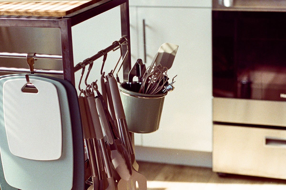 kitchen utensils hang from a prep counter in a sunlit kitchen