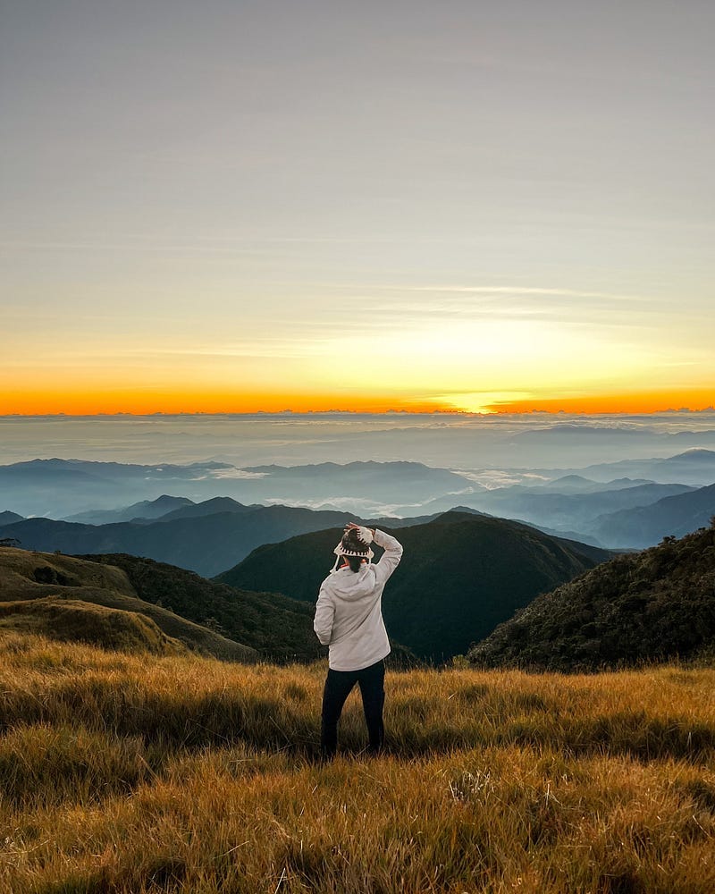 Girl staring out into the orange sunrise with a vast view of the mountains against a sea of clouds