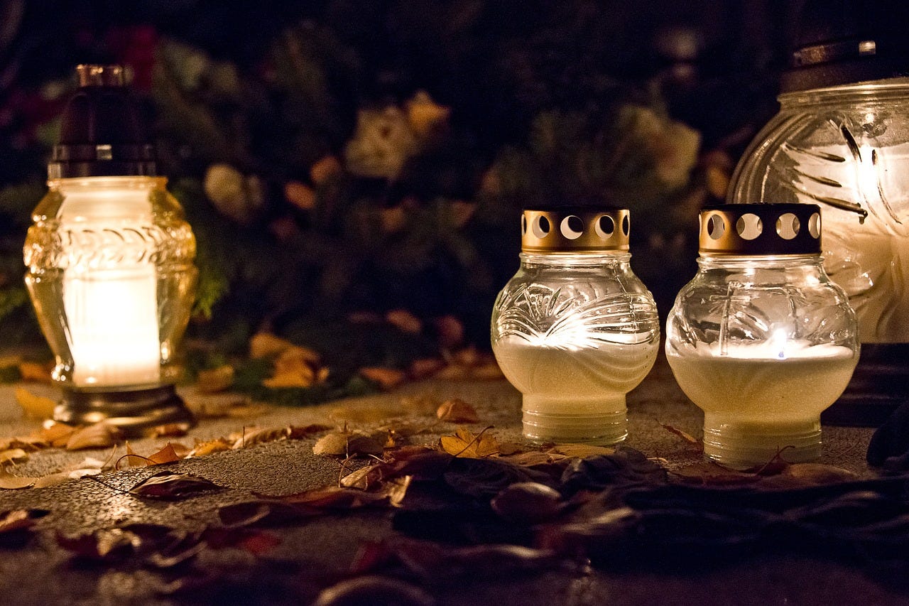 Four candles in glass lanterns burning in the dark with leaves around them