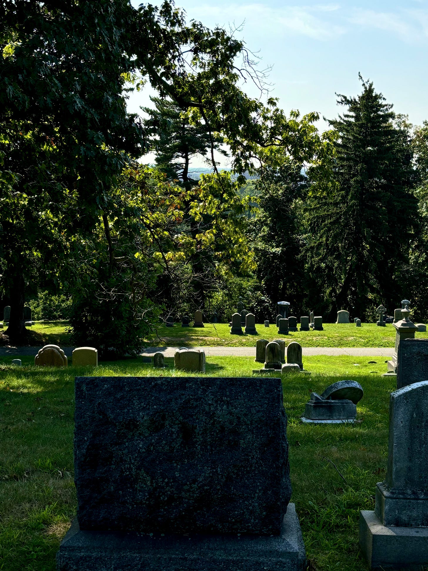 Looking out from a lush green hill. The near slope is planted with aged headstones.