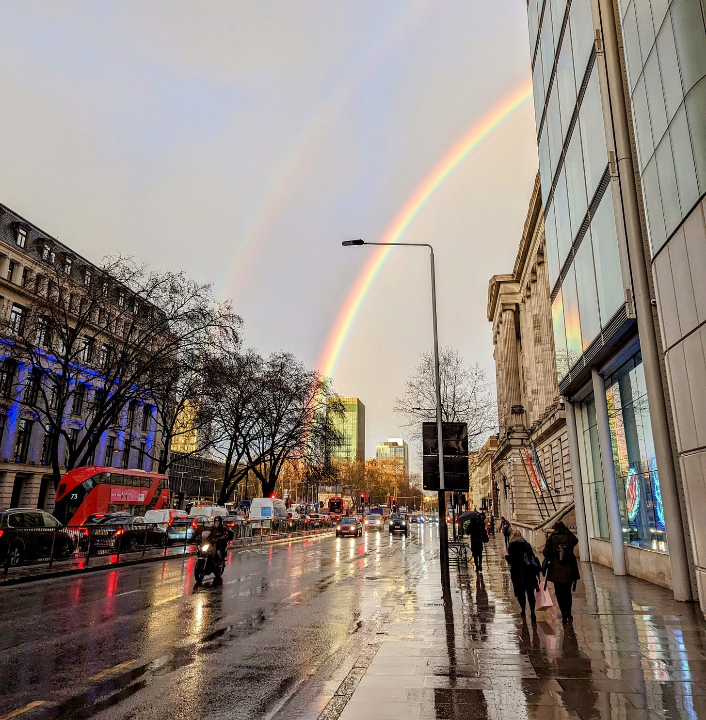 A photograph of a rainbow above a rain soaked London street. 