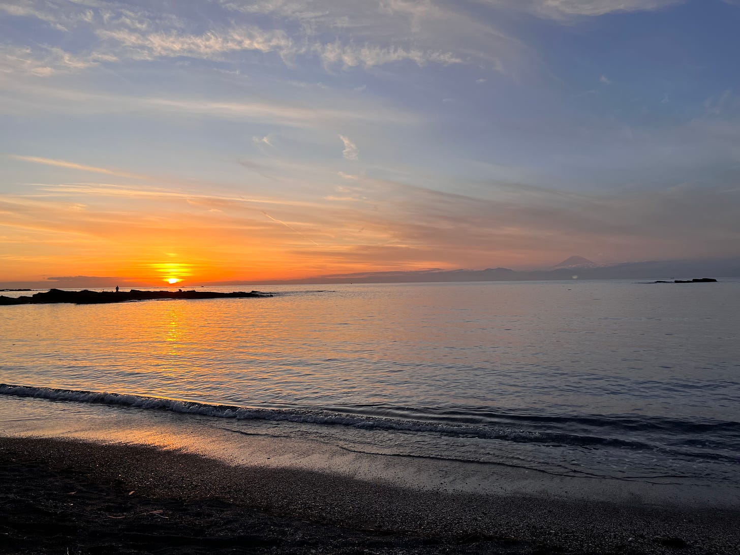 a sunset and a mountain on the horizon in the background with the sea in the foreground